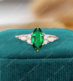 an emerald and diamond ring sitting on top of a velvet box