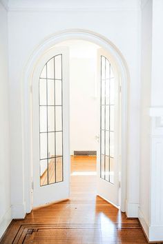 an open door leading into a white room with hardwood floors and arched doors on either side