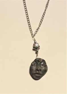 a necklace with a face on it and a diamond in the middle is hanging from a chain