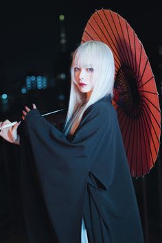 a woman with white hair is holding an orange and black umbrella in the night time