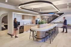 two people are standing in the kitchen next to an island with stools on it