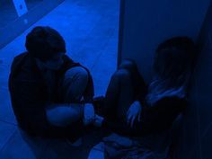 two people sitting on the floor in front of a wall with blue light behind them