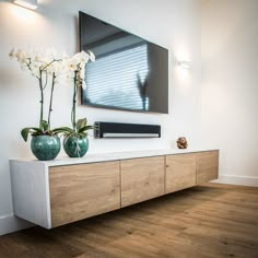 two vases with white flowers are sitting on a tv stand in the living room