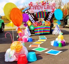 an outdoor birthday decoration with balloons and candy on the ground in front of a car