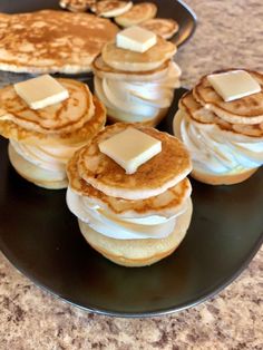 pancakes with butter and syrup on a black plate next to some other desserts in the background