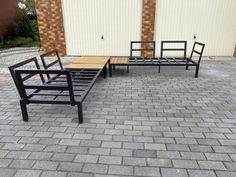 three black metal benches sitting on top of a brick floor next to a building with two doors