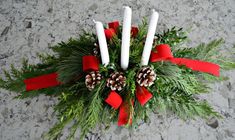 three white candles with pine cones and red ribbon