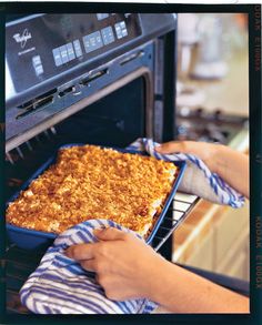 a person holding a dish in front of an oven with the door open to show it's baked casserole