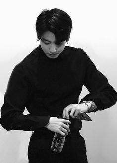 a man in black shirt cutting something with knife and scissors on white wall behind him