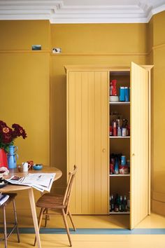 a dining room with yellow walls and wooden furniture in the center is a small table that has flowers on it