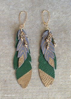 two pairs of green and gold leaf earrings on a white cloth covered surface with beads