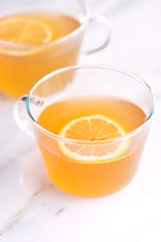 two glasses filled with orange juice sitting on top of a white counter next to an orange slice