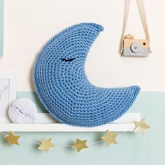 a crocheted blue crescent pillow sitting on top of a shelf next to pictures