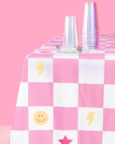 two cups on top of a table with pink and white checkerboard pattern, one has a smiley face