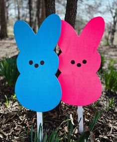 two wooden peeps sitting next to each other on top of the ground in front of trees