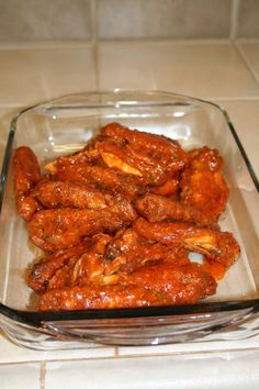 a glass dish filled with chicken wings on top of a tiled kitchen counter next to a knife