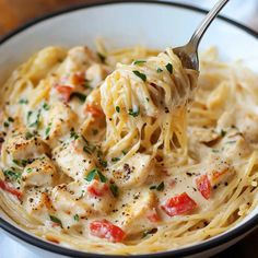 a spoon full of chicken alfredo with tomatoes and parmesan cheese in a white bowl