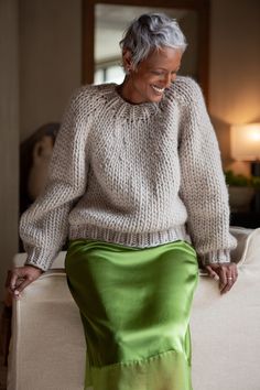 an older woman sitting on top of a couch wearing a green skirt and white sweater