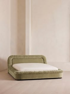 a green couch sitting on top of a wooden floor next to a white wall and window