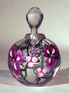 a glass bottle with pink flowers painted on the outside and inside, sitting on a white surface