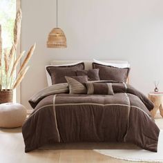 a bed with brown and white comforters in a room next to a plant on the floor