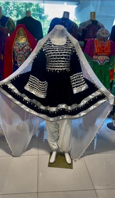 This stunning dress is made of black velvet with intricate white and black coin and lace embroidery. The embroidery is done in the traditional Kuchi style, which is characterized by its use of geometric patterns and bright colors. The dress is medium length and flowing, with a fitted bodice and a full skirt. It has long sleeves that are gathered at the wrists. The neckline is scoop-necked and decorated with a row of lace. The hem of the dress is also decorated with coins and lace. This dress is Traditional Velvet Dresses With Dabka Work, Embroidered Velvet Dress With Traditional Drape, Traditional Velvet Dress For Festivals, Traditional Velvet Dress With Dupatta, Black Dresses With Traditional Patterns For Festive Occasions, Black Festive Dresses With Traditional Patterns, Festive Black Dresses With Traditional Patterns, Festive Black Dress With Traditional Patterns, Black Dresses With Traditional Patterns For Eid