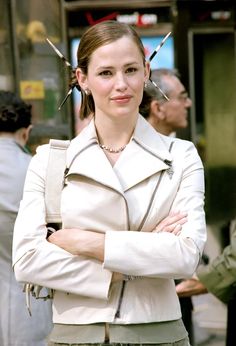 a woman standing with her arms crossed and looking at the camera while wearing a white jacket