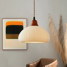 a white lamp hanging from a ceiling next to a brown chair and painting on the wall