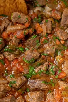 meat and vegetables cooking in a pot with a wooden spoon