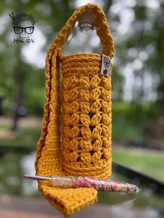 a crocheted water bottle holder hanging from a hook with a pen in it