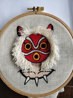 a red and white embroidered fox head with yellow eyes on a wooden hoop hanging from a wall