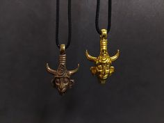 two necklaces with gold colored pendants hanging from black cords on a dark background