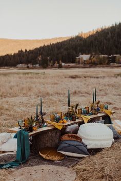 a table with candles and pillows on it in the middle of a dry grass field