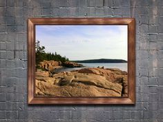 a frame hanging on a brick wall with a view of the ocean and rocky shore