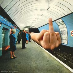 a person's hand pointing at something on the train platform with people standing around