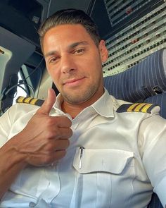 a man in uniform giving the thumbs up sign while sitting in an airplane with control panel behind him