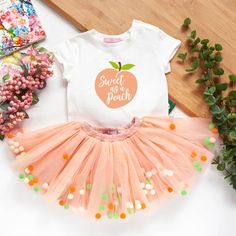 a white shirt with an orange and green apple on it, pink tutu skirt and some flowers