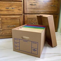 a cardboard box with files in it sitting on the floor next to a dresser and drawers