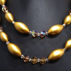 *Description: This is a beautiful mid-century necklace and earring set from the late 1950s. The colors and style are representative of this time period with the large metallic pearled finish oval beads with topaz Austrian Crystals as accent beads. The matching earrings have one crystal in the middle and six of the gold metallic beads around the center in a flower design. The necklace has aurora borealis rhinestone bars near each end. This is a great mid-century set to add to your favorite vintag Gold Beaded Necklaces For Evening, Gold Necklaces With Round Beads For Evening, Gold Beads Jewelry For Evening, Double Strand Polished Beads Jewelry For Party, Gold Round Beads Evening Jewelry, Evening Costume Jewelry Necklace With Faceted Beads, Gold Single Strand Beaded Necklace For Party, Handmade Gold Beaded Necklaces For Evening, Handmade Gold Beaded Necklace For Evening