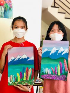 two girls are holding up paintings with masks on their faces and one girl is wearing a face mask