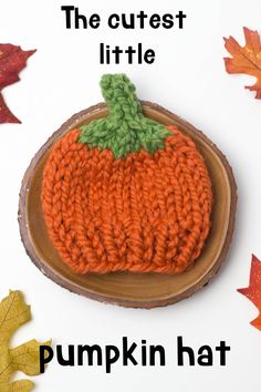 an orange knitted pumpkin hat sitting on top of a wooden slice with leaves around it