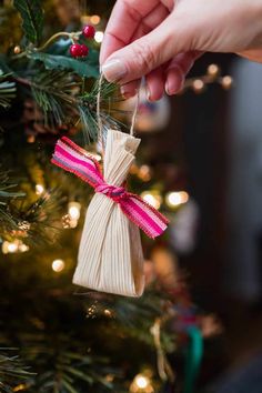 a hand holding a string ornament on top of a christmas tree