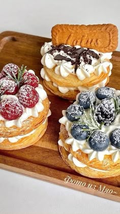 three pastries on a wooden platter covered in powdered sugar and fresh berries