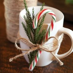 two mugs with candy canes tied to them sitting on a table next to twine of twine