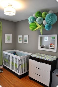 a baby's room decorated in green, white and grey with hanging paper lanterns above the crib