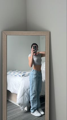 a woman taking a selfie with her cell phone in front of a bedroom mirror