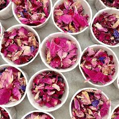 many white bowls filled with pink flowers on top of a cement floor and one bowl full of petals