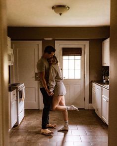 a man and woman standing next to each other in a kitchen with tile flooring