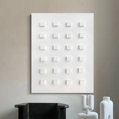 a white wall hanging on the side of a wall next to a chair and vase