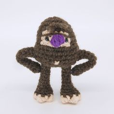 a crocheted stuffed animal with a purple ball in its mouth and hands behind it